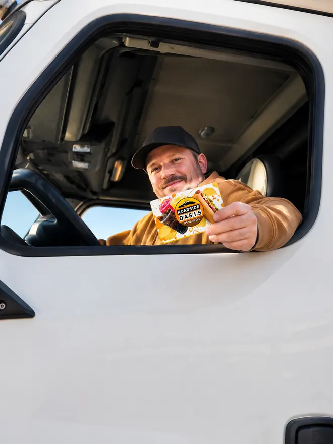Driver leaning out of his truck cab window holding a Roadside Oasis Rewards card in Menifee, CA