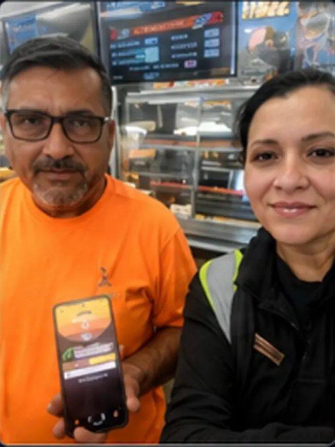 Customer in an orange shirt showing the Roadside Oasis app on his phone next to a store associate