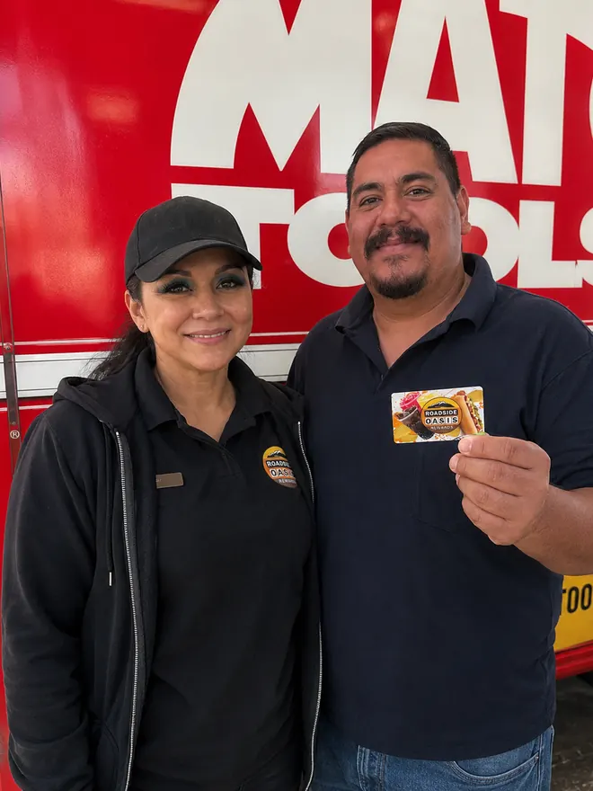 Roadside Oasis team member and a smiling rewards member holding his Rewards card outside the store in Menifee, CA